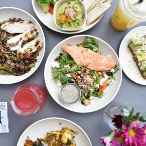 A variety of healthy weight loss meals featuring grilled salmon salad, lean chicken with wild rice, and roasted vegetables on a grey table.