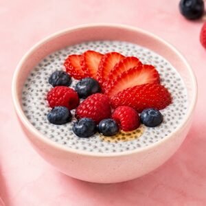 Chia seed pudding made with milk and topped with fresh strawberries blueberries raspberries and honey in a pink bowl