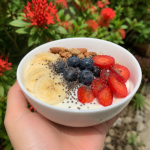 Greek yogurt bowl with fruits chia seeds and nuts held by hand in garden background for healthy high protein breakfast for weight loss