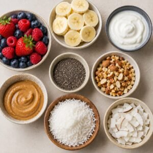 Healthy banana pancake toppings including fresh berries, sliced bananas, Greek yogurt, chia seeds, crushed nuts, peanut butter, and coconut flakes arranged in bowls.