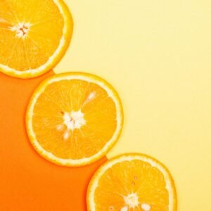 Fresh orange slices on a bright orange and yellow background, one of the Best Vitamin C Fruits for Glowing Skin.